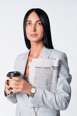 Business partner woman with cup of coffee and newspaper dressed in a modern light suit wearing the gold watch and having black manicure.