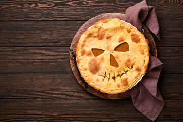 Halloween food. Homemade pumpkin pie or tart with a scary face for Halloween on a wooden table. Copy space. Halloween food concept.