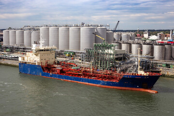 Oil tanker moored an oil terminal with fuel storage silos in an industrial port