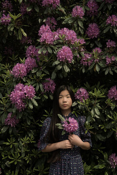 portrait of asian girl with pink rhododendron flowers near blossoming bush in spring