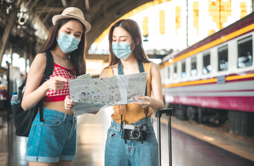 Fototapeta premium Asian backpack traveler people with camera standing at train station platform and waiting train arrivel, summer holiday travelling looking down at the map, travel concept.