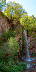 Beautiful waterfall on the mountain with blue sky shining sun. Waterfall in the mountains of the North Caucasus. Nature abstract background. Vertical format.