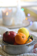 Silver bowl with various fruit, soft blanket and various Christmas decorations. Hygge at home. Selective focus.