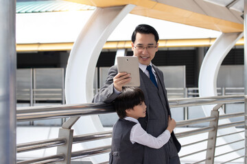 Asian businessman in a gray suit is teaching his son to learn business from an early age.