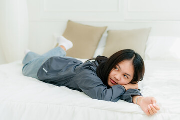 Portrait Asian cute long-haired teen wearing a gray long sleeve shirt Lay back and relax in bed in the bedroom happily.