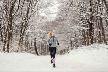 Obraz premium Happy fit sportswoman jogging in nature at snowy winter day. Healthy life, winter sport