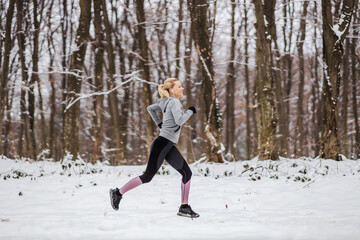 Slim sportswoman running in woods at snowy winter day. Cardio exercises, nature fitness, winter fitness