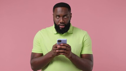 Irritated angry sullen young american man 20s wear green t-shirt using mobile cell phone get fake news unexpected rumor has some problems isolated on plain pastel light pink background studio portrait