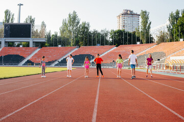 A large group of children, boys and girls, run and play sports at the stadium during sunset. A healthy lifestyle.