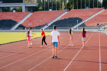 Fototapeta premium A large group of children, boys and girls, run and play sports at the stadium during sunset. A healthy lifestyle.