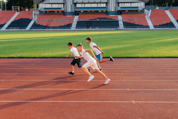 A large group of boys ' children are taught by a coach at the start before running at the stadium during sunset. A healthy lifestyle.