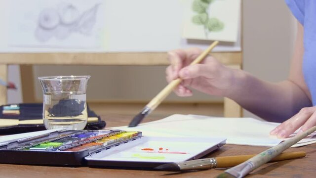 The artist applies watercolor paint to the brush and draws.