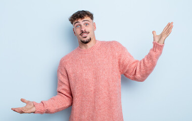 young handsome man shrugging with a dumb, crazy, confused, puzzled expression, feeling annoyed and...