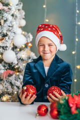 Santa little helper with decorative christmas tree on background. Little smiling boy make christmas...