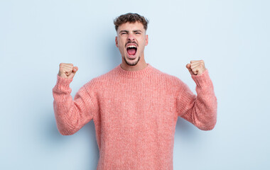 young handsome man shouting aggressively with an angry expression or with fists clenched celebrating success
