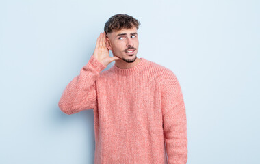 young handsome man looking serious and curious, listening, trying to hear a secret conversation or...