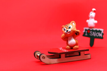 A toy tiger on a sled, a snowman in the background, on a red background. Place for text