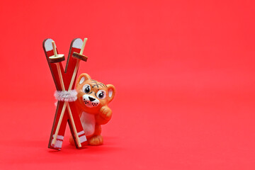 A toy tiger with skis in its paws, the year of the tiger 2022 on a red background, a place for text