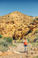 A woman with a backpack walks along a trail in a deserted canyon with red rocks. Hiking path and the dangers of solo trekking
