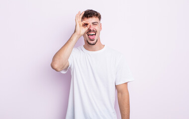 young handsome man smiling happily with funny face, joking and looking through peephole, spying on...
