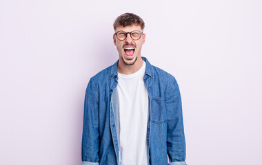 young handsome man shouting aggressively, looking very angry, frustrated, outraged or annoyed,...