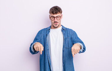 young handsome man with open mouth pointing downwards with both hands, looking shocked, amazed and...