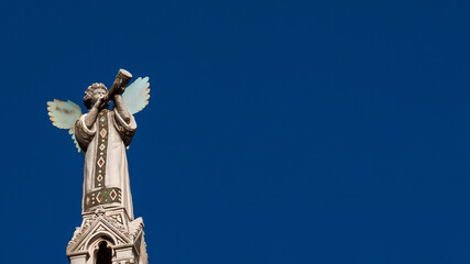Cherub Angel blowing trumpet. A medieval 13th century statue a the top of St Michael Church in...