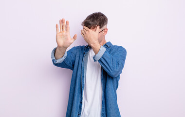 young handsome man covering face with hand and putting other hand up front to stop camera, refusing...