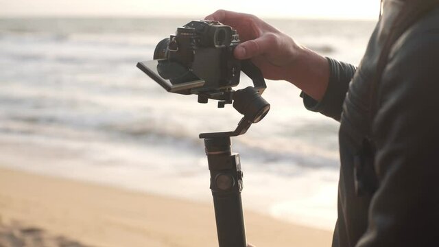 Filmmaker shoot video on camera with electronic stabilizer on the beach at sunrise 
