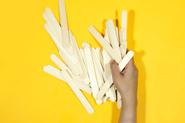 hand holding wooden sticks isolated on yellow background to use for epilation o medical checkup