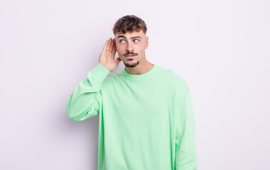 young handsome man looking serious and curious, listening, trying to hear a secret conversation or...