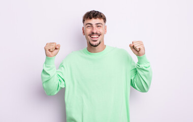 young handsome man feeling happy, positive and successful, celebrating victory, achievements or...