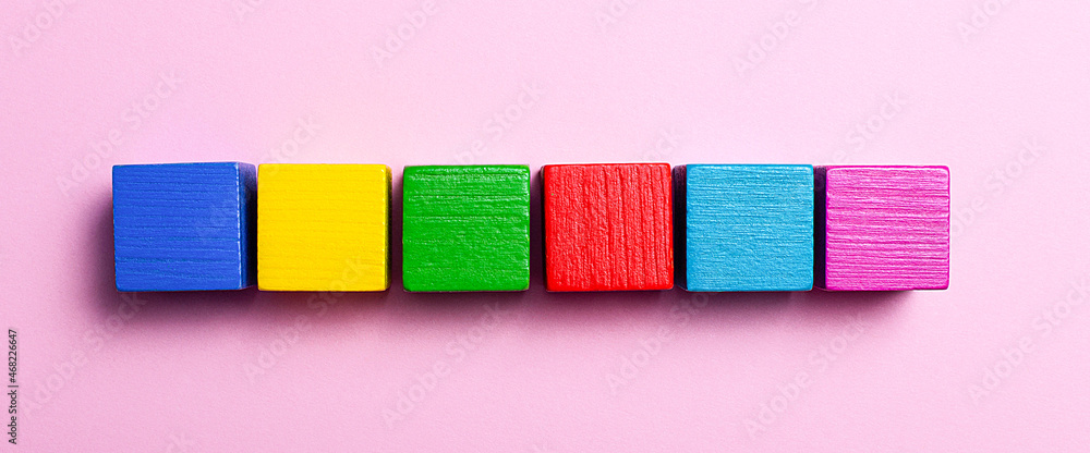 Poster on a light pink background in a row of multi-colored wooden cubes with a place to insert text. copy 