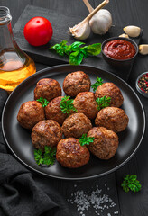 Meatballs with fresh basil close-up on a dark background with spices, oil and garlic.