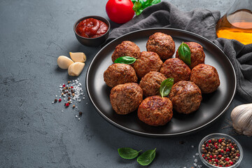 Delicious meatballs in a black plate on a background of sauce, spices and garlic.