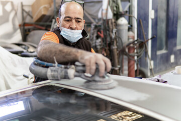 Auto mechanic sanding a part of a car in a garage. Preparing for painting the car in a workshop