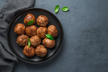 A plate with meatballs and basil on a dark background.