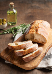 Italian fresh ciabatta bread cut  slices with rosemary and olive oil on wooden background. Close up and copy space