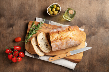 Fresh italian ciabatta bread cut  slices with tomato, rosemary and olive oil on wooden background. Top view  and copy space