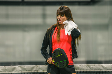 Beautiful girl playing paddle tennis, racket in hand wipes the sweat. Young sporty woman at the end of the match. Sweaty padel athlete ready to take shower. Sport, health, youth and leisure concept