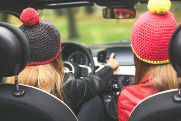 Trendy girls sitting in the car. Teen in front of the steering wheel with a friend beside. Young...