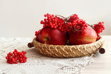 Autumn still life: branches of viburnum with red berries on red apples in a decorative vase, next to a gray napkin, side view, space for text