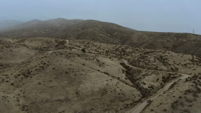 Aerial drone flying over barren mountains in Boise, Idaho on a foggy afternoon following a SUV.