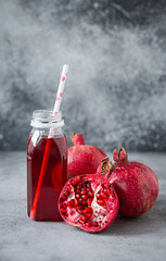 Freshly squeezed red pomegranate healthy juice in bottle with paper straw near whole and split in...