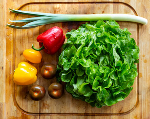 A washed set of vegetables: green salad, pepper, kumato tomatoes and leek for a salad ready on a cutting board