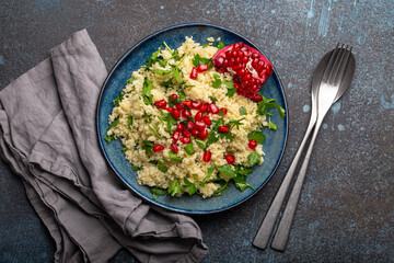 Bright colourful couscous or bulgur salad with pomegranate seeds Tabbouleh in rustic blue ceramic bowl top view on concrete background, traditional middle eastern or arab dish
