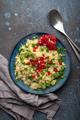 Bright colourful couscous or bulgur salad with pomegranate seeds Tabbouleh in rustic blue ceramic bowl top view on concrete background, traditional middle eastern or arab dish
