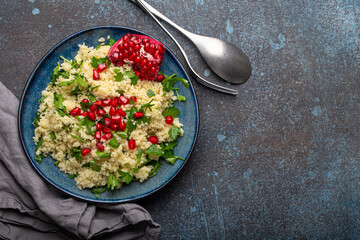 Bright colourful couscous or bulgur salad with pomegranate seeds Tabbouleh in rustic blue ceramic bowl top view on concrete background, traditional middle eastern or arab dish with space for text
