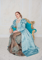 Beautiful woman in medieval style blue dress sitting in the armchair.