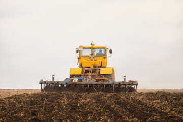 Fototapeta premium Tractor pulls disc harrow. Soil cultivation. Back view.
